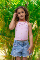 Young girl in a pink top and denim shorts standing in front of green palm leaves.