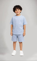 Child wearing a light blue outfit with shorts on a gray background